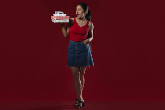 Teenage girl standing with gift boxes against maroon background