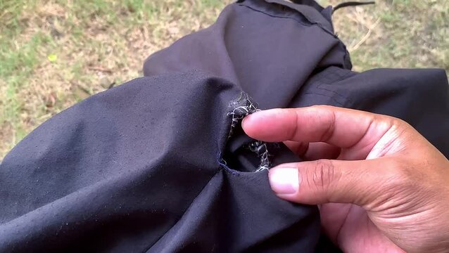 Fingers sticking out through a torn hole on black pants seam. broken pants.