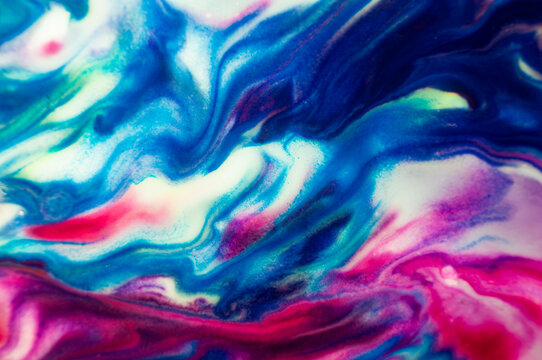 Swirling colors create patterns and shapes in blue, pink, and white on a canvas