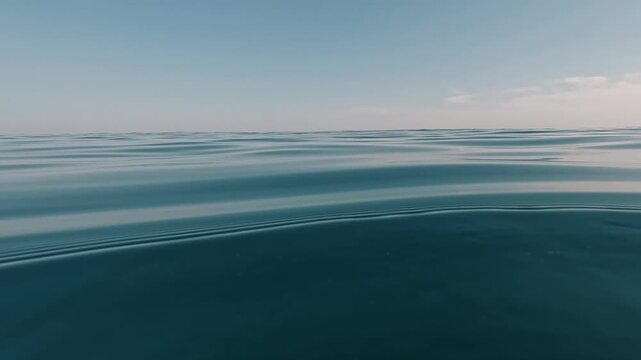 V&iacute;deo grabado a ras de agua en mar abierto, con un paddlesurfista pasando por delante de la c&aacute;mara sobre una tabla de paddle surf y cayendo al agua al final del clip. La escena muestra un entorno mari