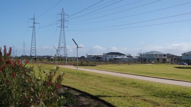 Large steel high-voltage electricity transmission towers and power lines run parallel to a public reserve and pedestria path in suburb of Tarneit, Melbourne Australia. Family homes borders easement