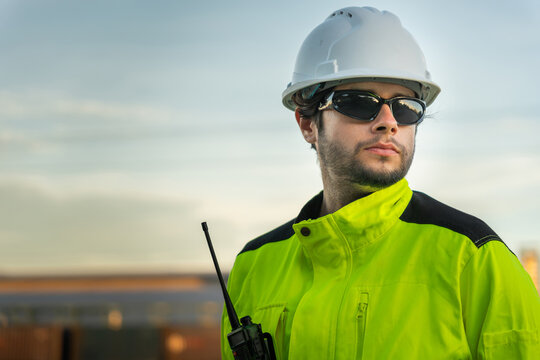 Portrait of professional engineer in safety gear at oil refinery, Industrial worker with hard hat and radio at oil and gas plant, Construction supervisor in high-visibility jacket at refinery site