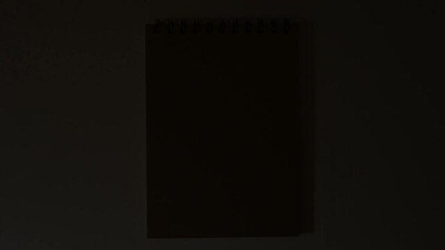 Blank spiral notebook on white surface with dramatic light transition