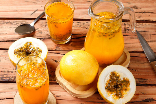 Fresh passion fruit juice in glasses and pitcher with whole and sliced passion fruits arranged on a rustic wooden table with kitchen utensils.