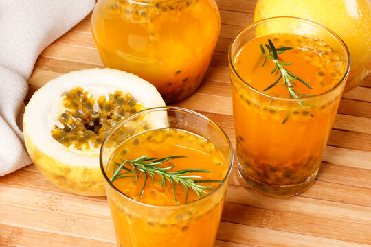 Two glasses of fresh passion fruit juice served with a glass pitcher and sliced tropical fruit on a wooden surface.