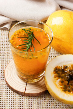Glass of fresh passion fruit juice with natural pulp and rosemary garnish served beside ripe passion fruit.