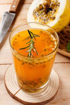 Fresh passion fruit juice with natural pulp served in a glass with rosemary garnish beside sliced tropical fruit.