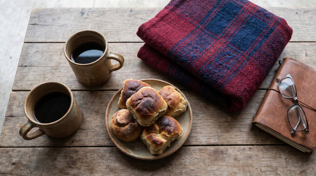 Two clay mugs of coffee with sweet bread and a folded textile on a rustic wooden table