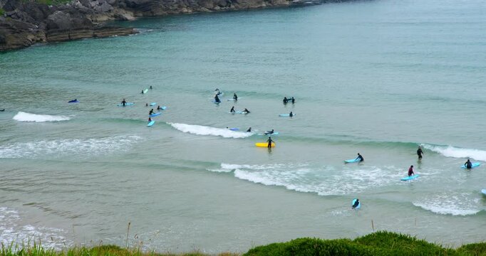 Surfers Ride the Waves: A group of surfers of varying skill levels enjoy a day of surfing at a scenic beach, with gentle waves rolling onto the shore and lush greenery framing the coastline.