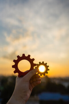 Hand holding wooden gears against the sunset sky. Concept of business strategy, cooperation, teamwork, efficient process, and engineering solutions for successful project management and development.