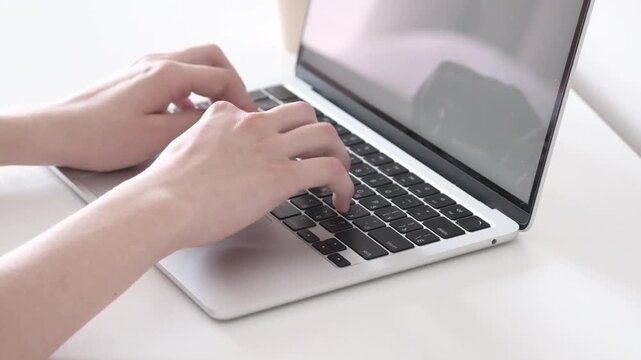 Hands typing on open laptop with blank bright screen in minimalist workspace, showing steady keyboard use on white desk with soft neutral light, clean modern composition for office tasks and online