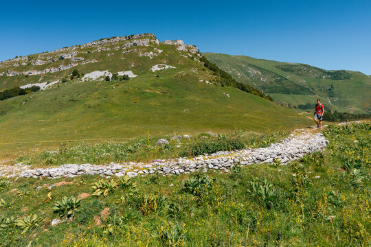 Hiker walking on a mountain trail, outdoor adventure lifestyle in a green alpine landscape. San Valentino di Brentonico, Monte Baldo Natural Park, Brentonico, Trentino, Italy.