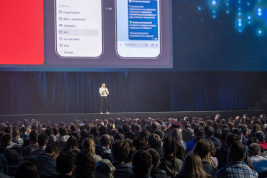 Conference speaker on stage delivering tech presentation to large attentive audience, professional event atmosphere, networking, education, public speaking, seminar.