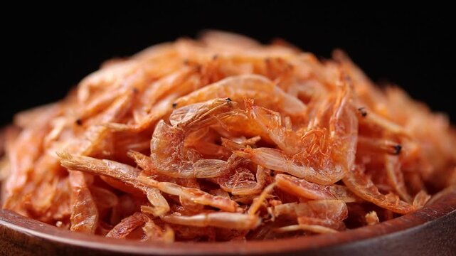 small dried salted shrimp in a wooden bowl slowly rotating on a black background.