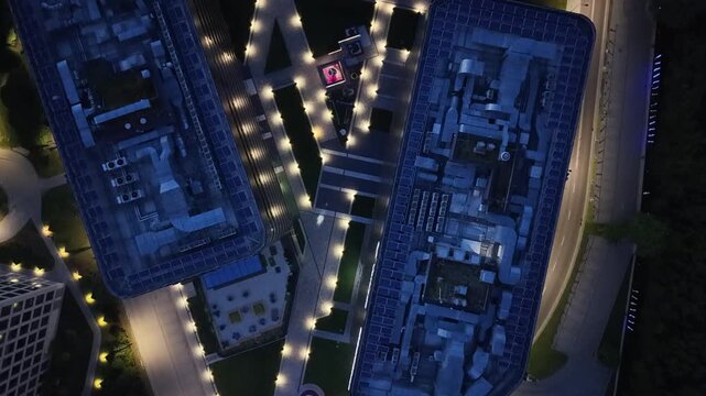 Aerial view of modern business center buildings illuminated at night, showcasing intricate architectural designs and surrounding landscaped areas with vibrant lighting and pathways