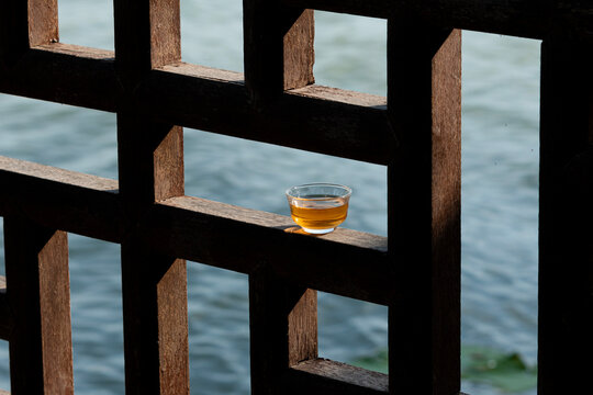 Glass teacup on a traditional wooden window frame with rippling water background.