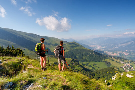 Active couple hiking with backpacks and poles on a mountain ridge during a summer adventure in Monte Baldo Natural Park, Brentonico, Trentino, Veneto, Italy.