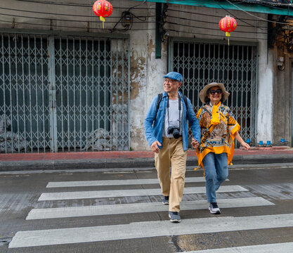 Couple walks hand in hand across a street with red lanterns in an urban area during daytime