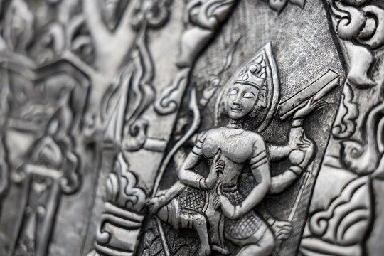 Ancient silver bas relief panel featuring seated deity carving with ornate floral motifs and textured metalwork conveying calm and reverence in close up detail