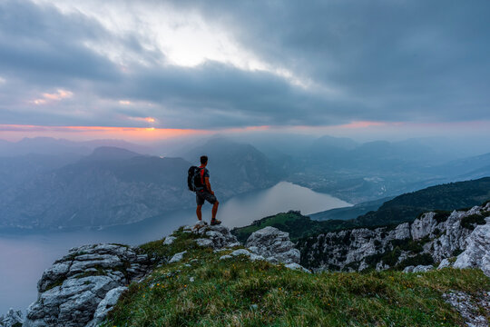 Hiker with backpack standing on a rocky peak during sunset for an outdoor adventure lifestyle, Altissimo Refuge "Damiano Chiesa", Monte Baldo Natural Park, Brentonico, Trentino, Veneto, Italy.