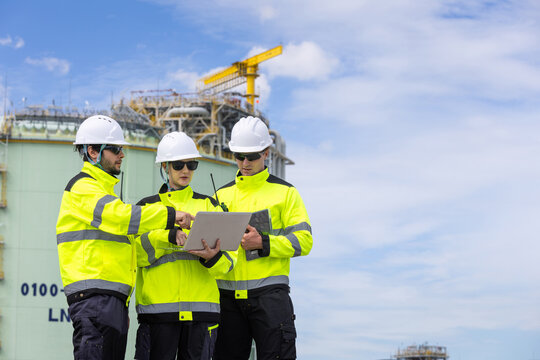 Engineering team with laptop at LNG terminal facility, Technicians in safety gear discussing project at natural gas plant, Industrial workers monitoring and planning operations at LNG storage site