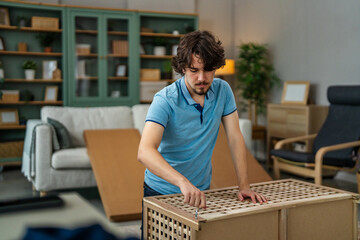 Fototapeta premium Young man assembling new flat pack furniture in living room