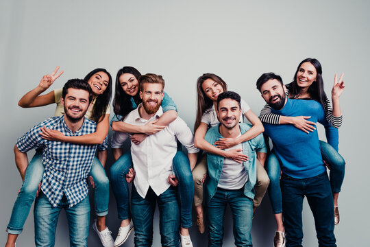 Happy group of young friends giving piggyback rides and posing together for a casual studio portrait celebrating friendship and fun