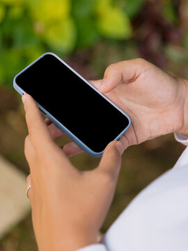 Hand holding smartphone with blank screen against outdoor background