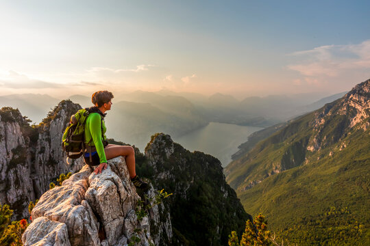 Hiker resting on a mountain edge enjoys a panoramic sunset view, highlighting travel adventure and lifestyle in Monte Baldo Natural Park, Ventrar trail, Brentonico, Trentino, Veneto, Italy.