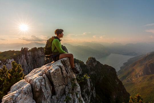 Hiker resting on a mountain edge enjoys a panoramic sunset view, highlighting travel adventure and lifestyle in Monte Baldo Natural Park, Ventrar trail, Brentonico, Trentino, Veneto, Italy.