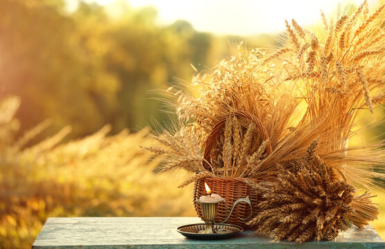 candle in candlestick and ripe grain ears close up on table in garden, sunny natural background. symbol of summer end, autumn season, harvest time. ceremony for Lammas, Lughnasadh wiccan holidays