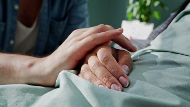 Man takes hand of beloved wife severe patient lying in bed