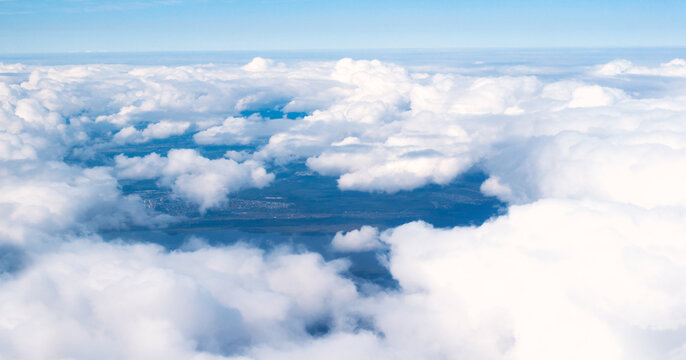 Aerial cloudscape, scenic blue sky background of a thick white cumulus clouds under a clear blue sky, as seen from an airplane window, panoramic view