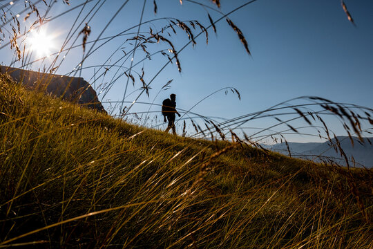 Hiker with backpack walking on a grassy mountain path for outdoor adventure and travel lifestyle in Monte Baldo Natural Park, Brentonico, Trentino, Veneto, Italy.