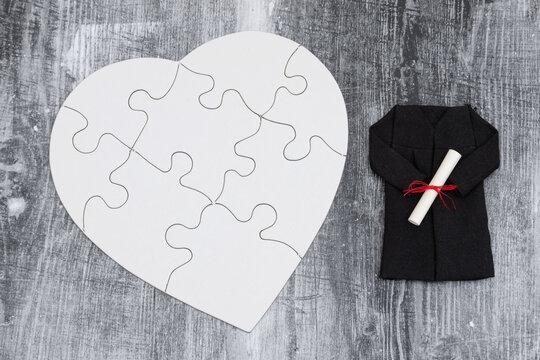 Blank white puzzle heart with grad gown and diploma on weathered wood for student loans