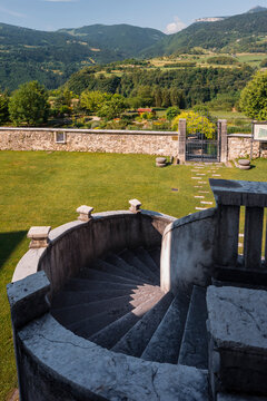 Stone spiral staircase overlooking a garden and mountain landscape for travel exploration at Monte Baldo Natural Park, Palazzo Baisi e Giradino dei Semplici, Brentonico, Trentino, Veneto, Italy.