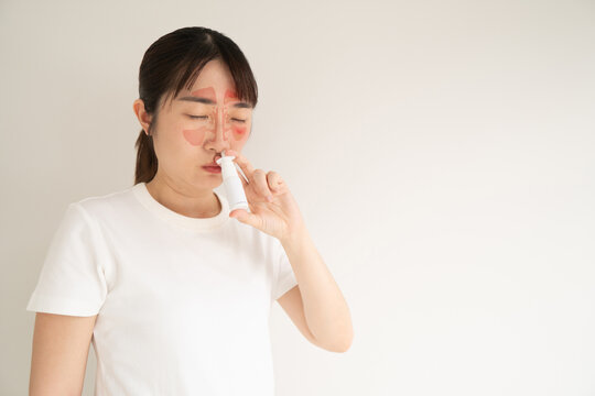 Asian woman face with nasal sinuses anatomy using nasal spray suspension for relieve symptoms such as sneezing, runny or itchy nose. Medical device used to treat allergic rhinitis.