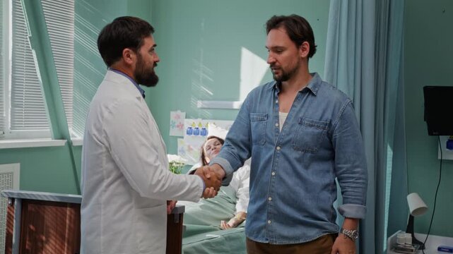 Doctor greets male visitor near patient bed in hospital