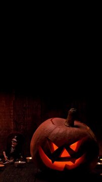 Halloween pumpkin with scary face and candles on dark background. Jack-o-lantern on black background. Vertical footage