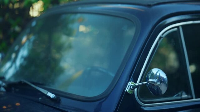 Close up of a vintage dark blue classic car windshield and chrome side mirror