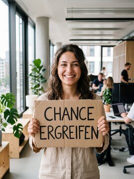 L&auml;chelnde junge Frau h&auml;lt Pappschild mit der Aufschrift Chance ergreifen im modernen B&uuml;ro