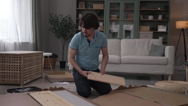 Young man assembling new wooden furniture at home