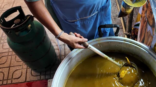 Close-up of a street food vendor ladling traditional Thai curry from a large cooking pot into a serving bowl at a local market in Thailand. Authentic Thai street food being prepared for takeaway. 4K v