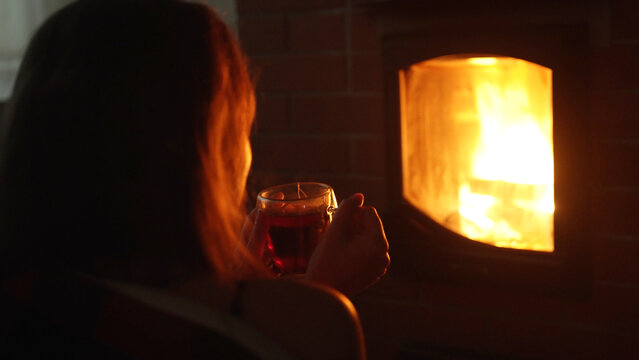 Woman holding cup of hot tea by cozy burning fireplace.