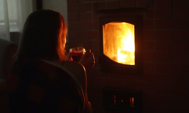 Woman holding cup of hot tea by cozy burning fireplace.