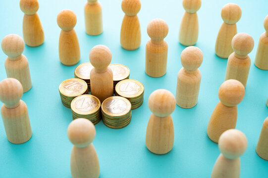 Concept of wealth concentration, economic inequality, and privilege represented with wooden pawns and stacks of coins.