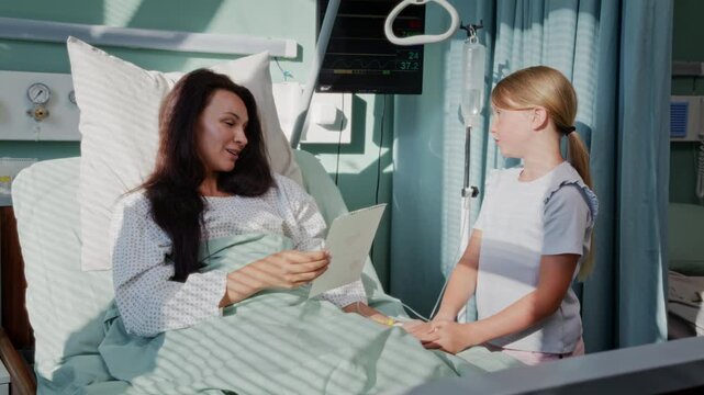 Girl gives handmade card to mother resting in hospital bed