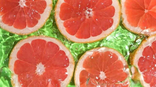 Slow motion of fresh grapefruit slices under rippling water with bubbles