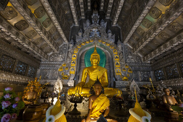 Obraz premium Golden Buddha statue seated in ornate silver temple interior with intricate carvings, lotus offerings and ceremonial decorations conveying serene sacred atmosphere and cultural reverence