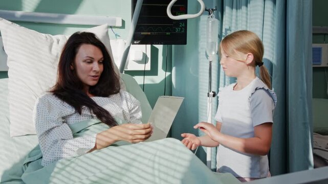 Daughter presents greeting card to ill mother in hospital ward